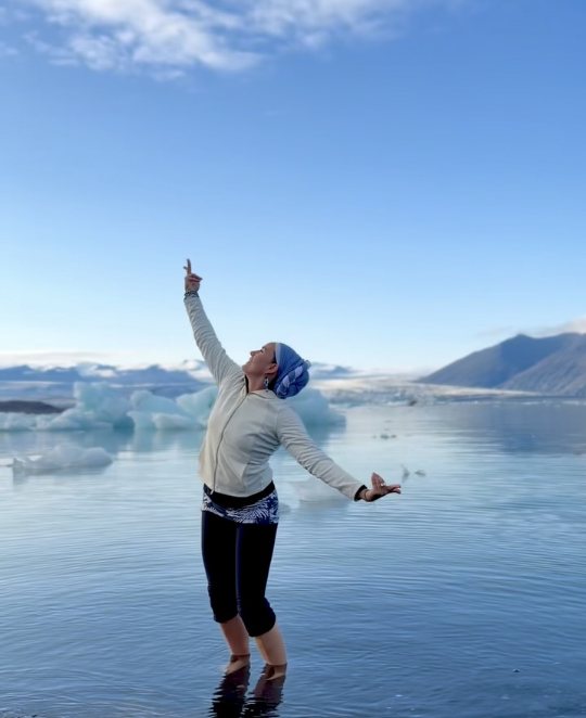 María con los brazos al cielo en un lago glaciar